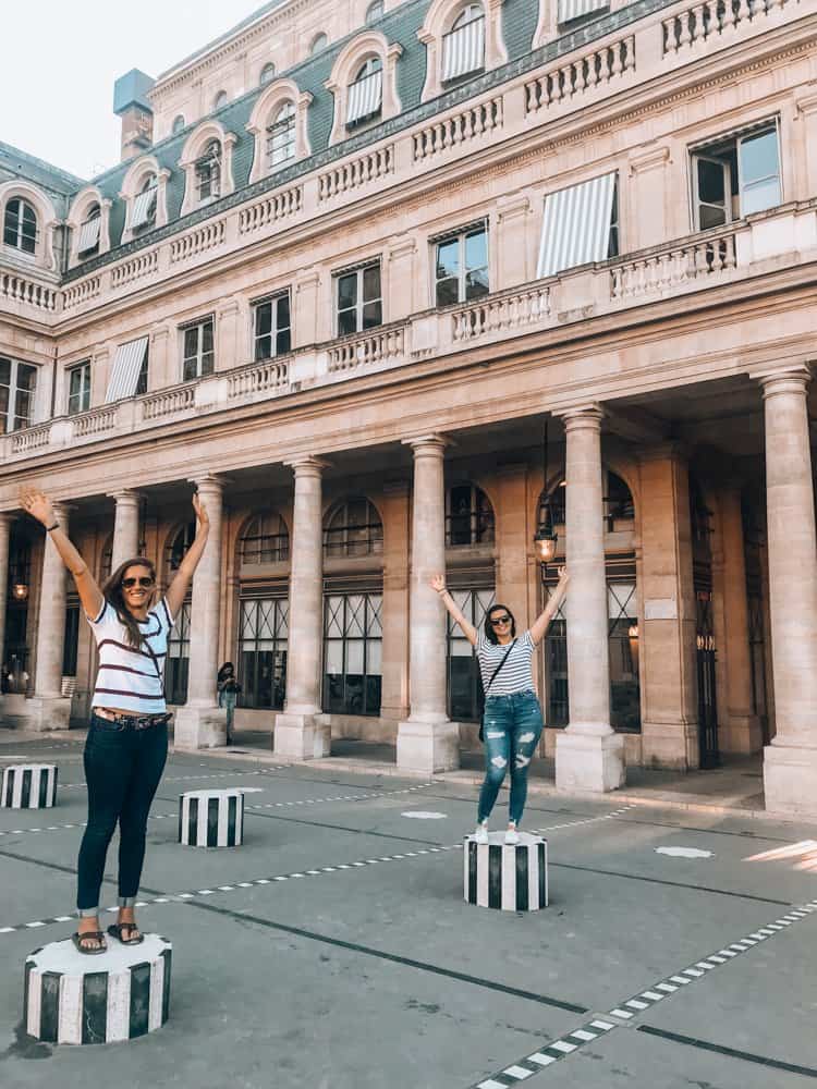 Kat and Alice posing with their hands in the air on the columns at Palais Royale