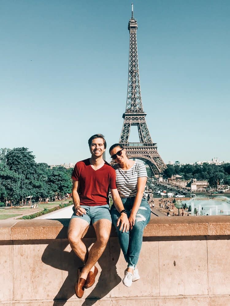 Kat and Chris sitting on a ledge in front of the Eiffel Tower in a portrait shot