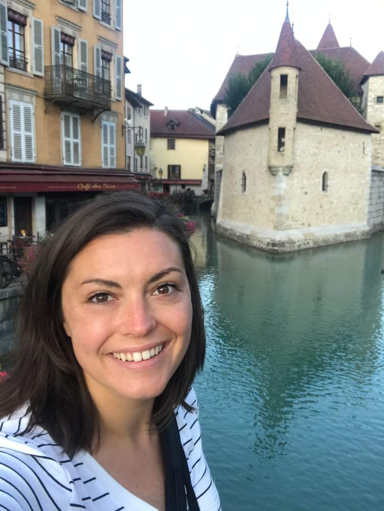 Kat smiling at the camera in front of Palais de l'isle in Annecy