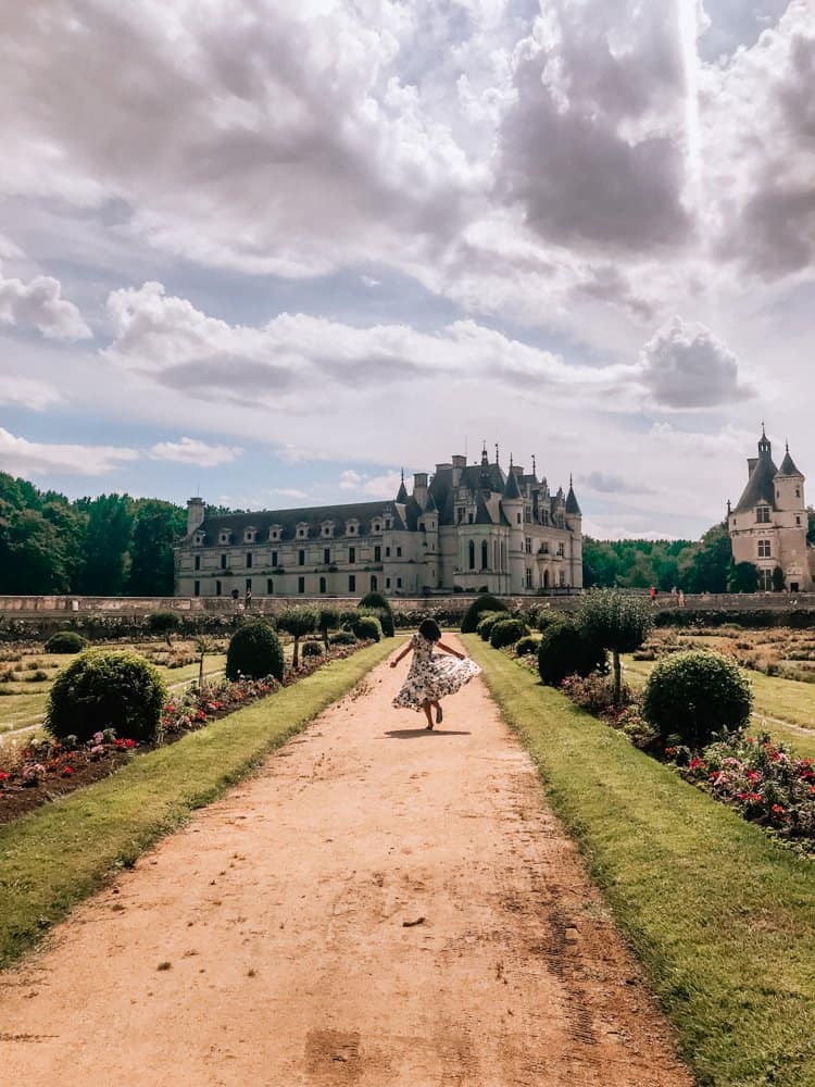 Kat twirling in a white patterened dress in front of Chateau de Chenonceau