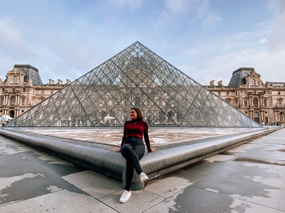 Kat sitting by the fountain at the Louvre in a wide angle shot