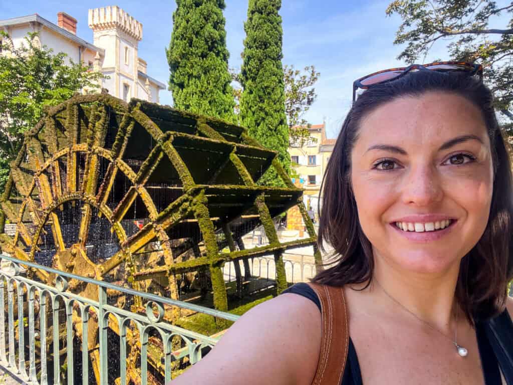 Kat smiling with a waterwheel in the background in L'Isle-sur-la-Sorgue