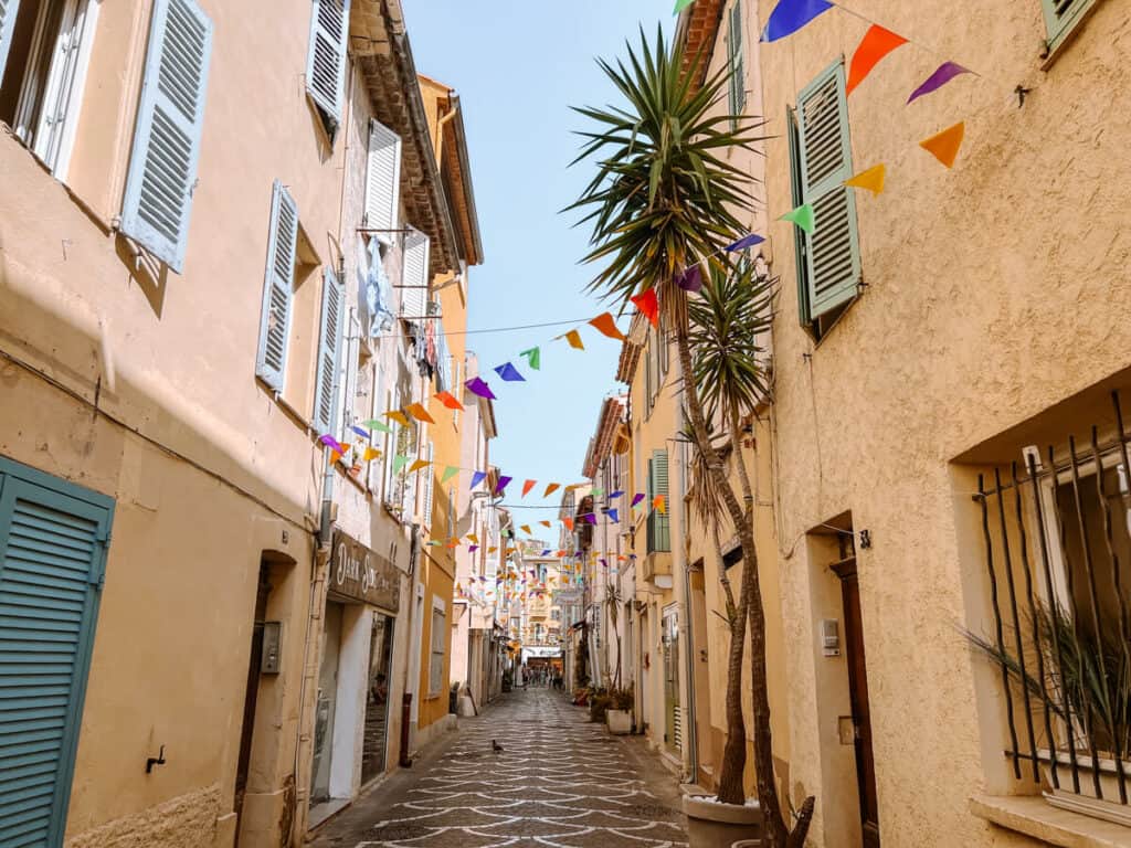 Street with light yellow buildings with flags over it in Antibes 2