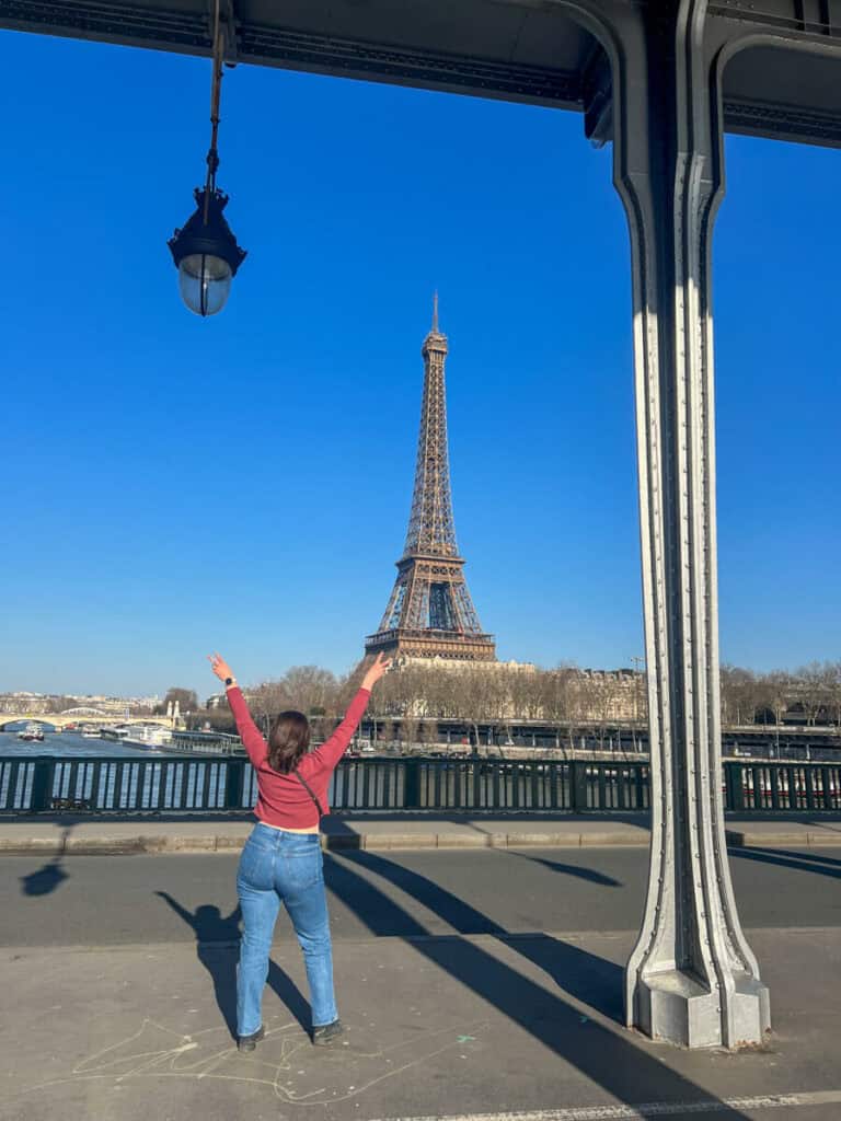 Kat with her back facing camera and peace fingers up under Pont de Bir-Hakeim with Eiffel Tower in the background