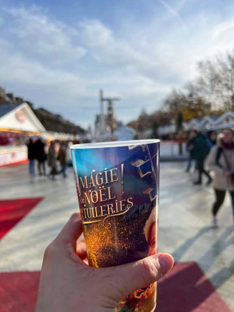 Tuileries Christmas market with mulled wine cup in foreground being held by a hand